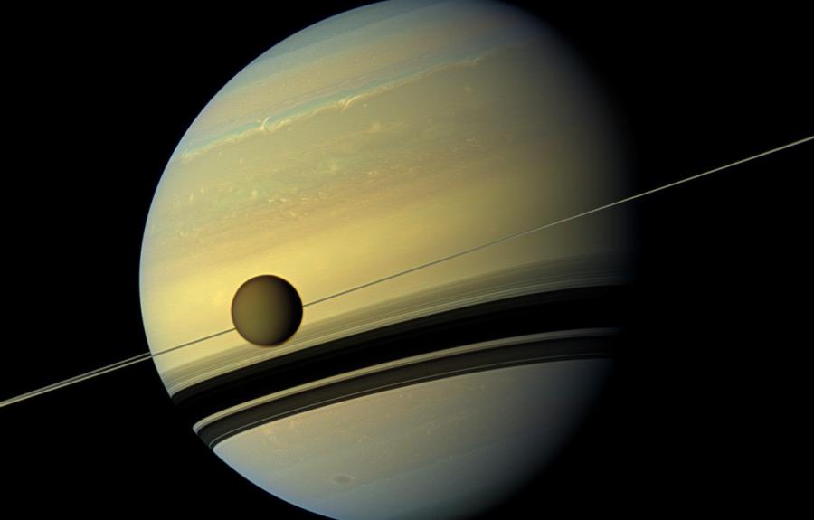 Titan, Saturn's largest moon, crosses the rings and the planet.